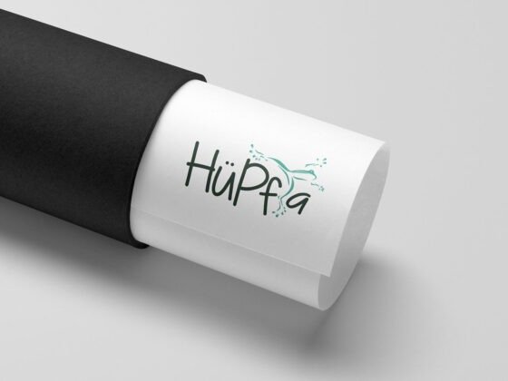 Eine weiße, aufgerollte Bahn mit "HüPfa" und grünem Springer steckt teils in einer schwarzen Röhre. Eine weiße, aufgerollte Bahn mit "HüPfa" und grünem Springer steckt teils in einer schwarzen Röhre.